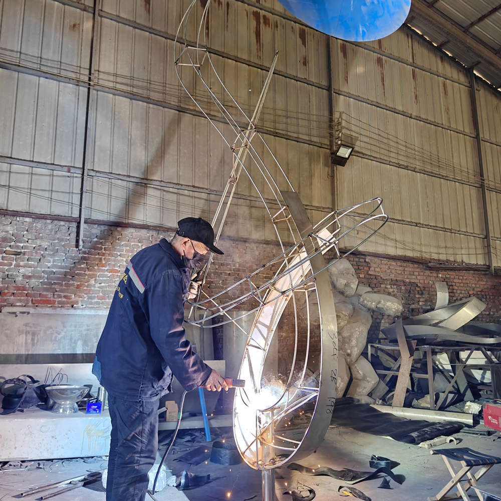 Craftsman welding the internal structure of stainless steel abstract sculpture
