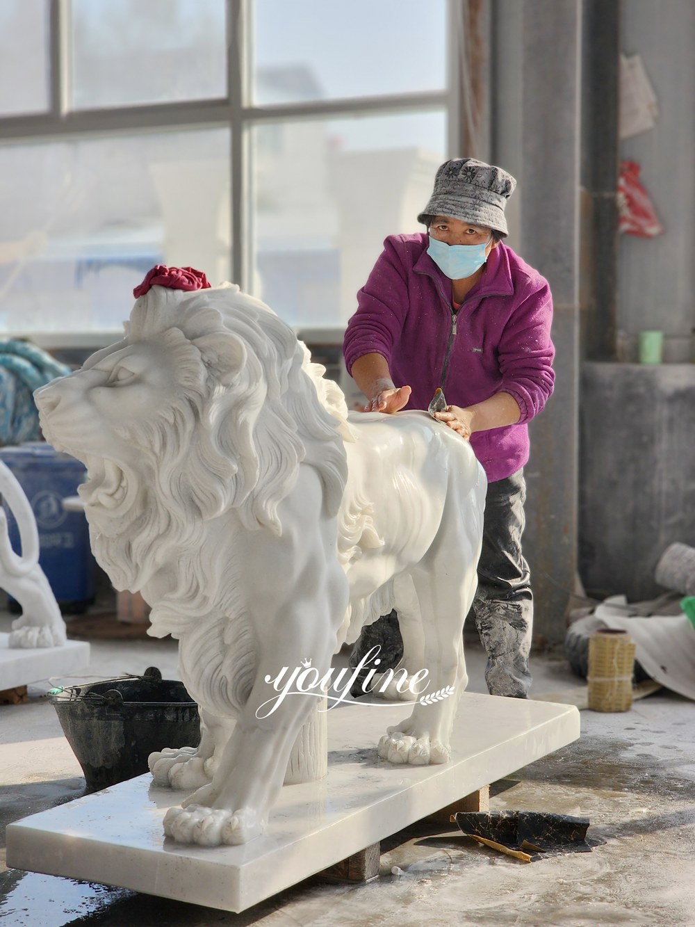 Un artigiano lucida una grande scultura in marmo bianco raffigurante un leone ruggente che cammina, all'interno di uno studio in fabbrica.
